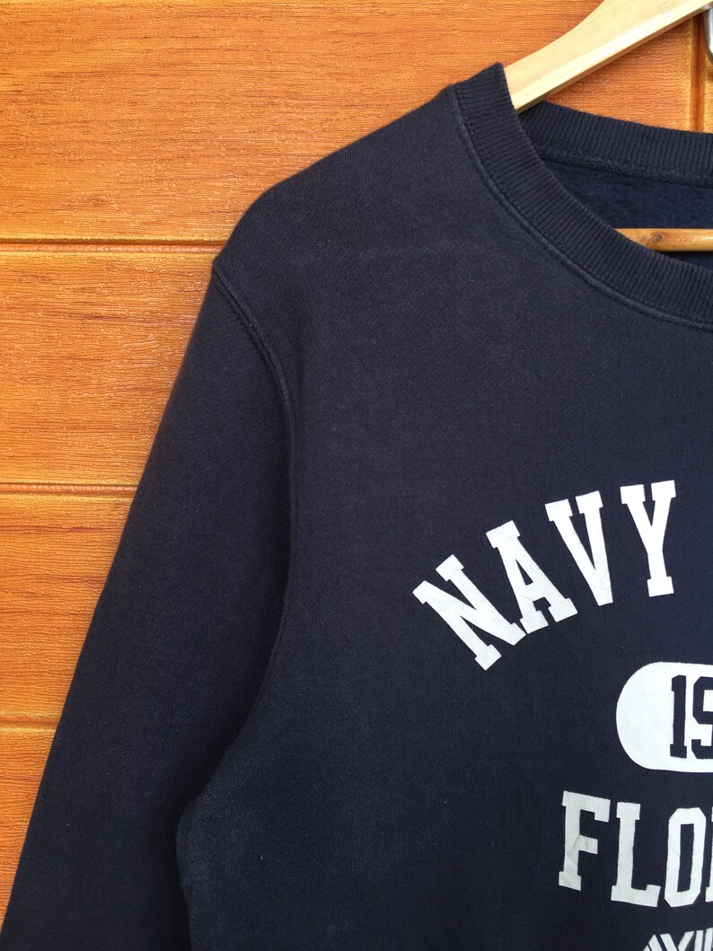 May include: A navy blue sweatshirt with white text that reads "NAVY" and "FLORIDA" with a white circle containing the number "19" in the centre.