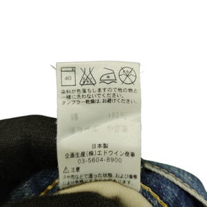 Puede incluir: Primer plano de una etiqueta blanca con texto japon&eacute;s y s&iacute;mbolos de cuidado. La etiqueta incluye instrucciones de lavado, una composici&oacute;n de tejido del 100% e informaci&oacute;n del fabricante. La etiqueta est&aacute; adherida a unos vaqueros azules.