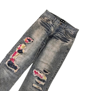 Könnte beinhalten: Blaue Jeans aus abgewetztem Denim mit bunten Stoff-Patches, die auf die Beine genäht sind. Die Jeans haben mehrere Risse und Löcher.