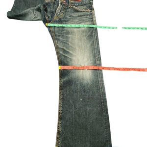 May include: Faded blue denim jeans with a distressed look. The jeans are measured with a green, red, and blue measuring tape. The waist measures approximately 16 inches, the inseam is 30 inches, and the leg opening is 13 inches.