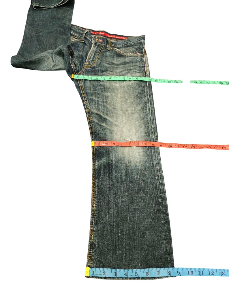 May include: Faded blue denim jeans with a distressed look. The jeans are measured with a green, red, and blue measuring tape. The waist measures approximately 16 inches, the inseam is 30 inches, and the leg opening is 13 inches.