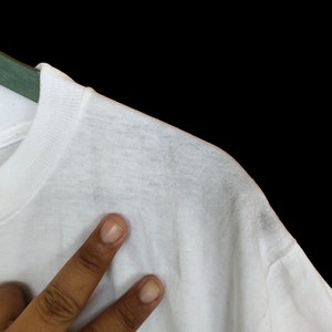 May include: White t-shirt with a smooth texture. The shirt is hanging on a hanger.