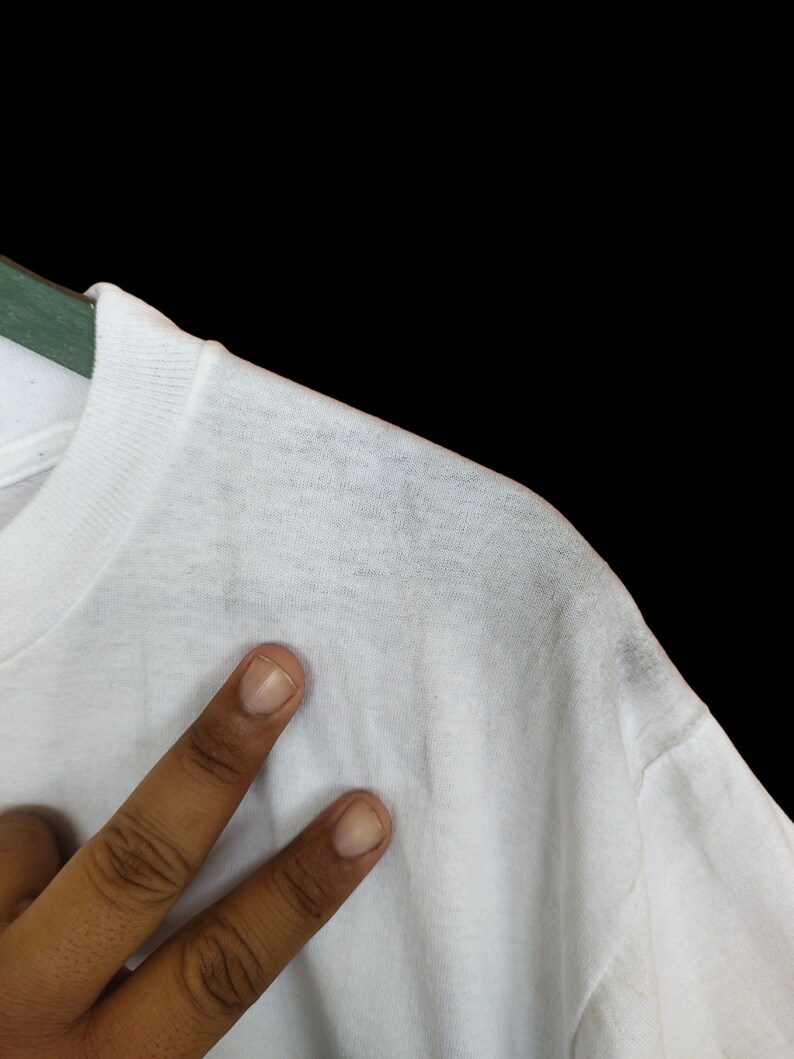 May include: White t-shirt with a smooth texture. The shirt is hanging on a hanger.