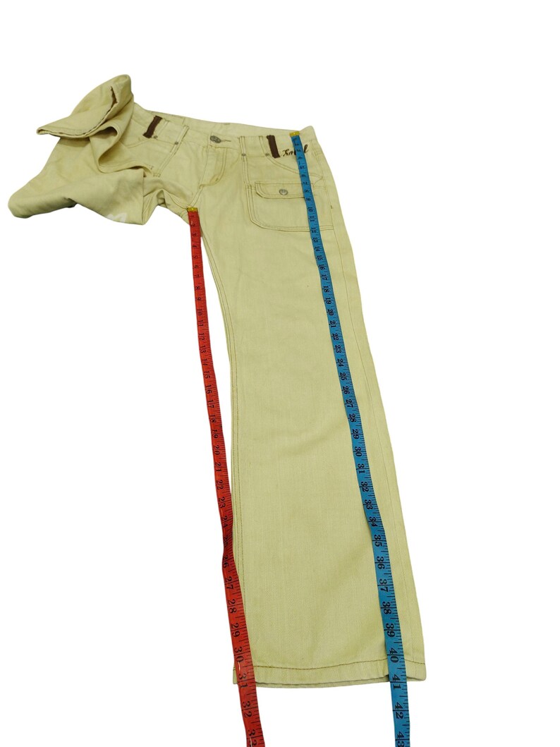 Puede incluir: Vaqueros de mezclilla amarillo claro con costuras y detalles marrones. Los vaqueros tienen un dise&ntilde;o cl&aacute;sico de cinco bolsillos y una pernera recta. La longitud total es de aproximadamente 107 cm.
