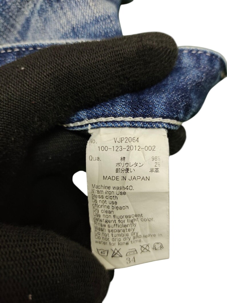 May include: Close-up of a denim garment tag with the text "VJP2064" and care instructions. The tag indicates the garment is made in Japan and includes washing and ironing guidelines. The size is indicated as 34.