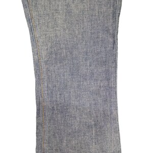 May include: Close-up of the denim fabric of a pair of blue jeans. The fabric has a subtle texture and a light blue color.