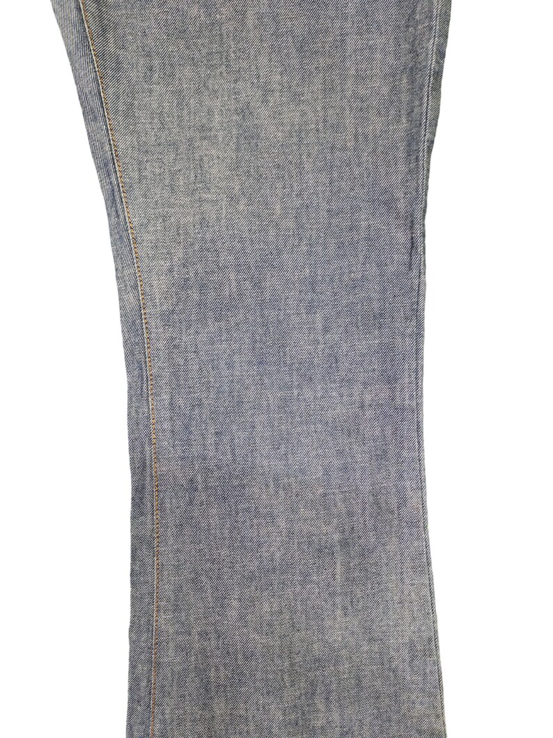 May include: Close-up of the denim fabric of a pair of blue jeans. The fabric has a subtle texture and a light blue color.