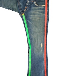 May include: A pair of blue denim jeans with a red and green measuring tape along the side seams. The jeans have a bootcut style and are in good condition.