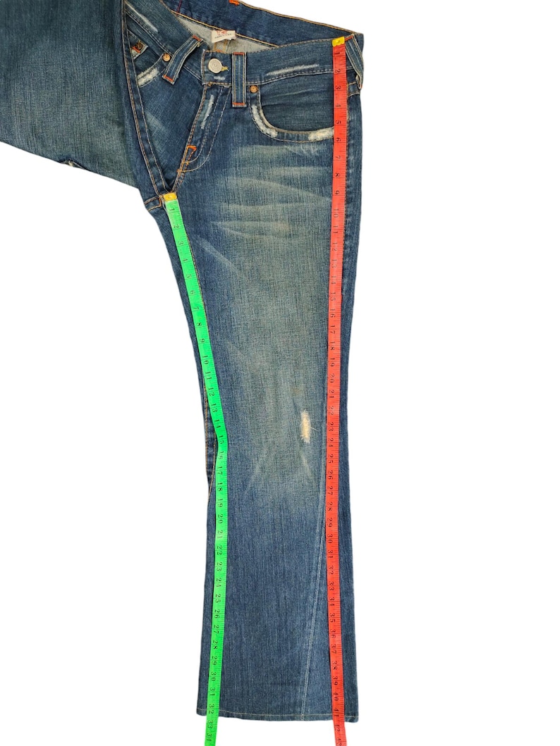 May include: A pair of blue denim jeans with a red and green measuring tape along the side seams. The jeans have a bootcut style and are in good condition.