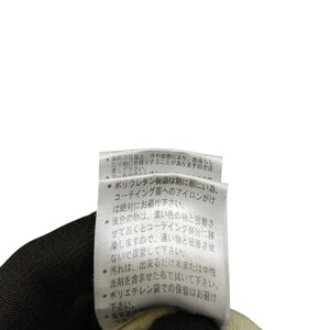 Puede incluir: Primer plano de una etiqueta de ropa con texto en japon&eacute;s. La etiqueta blanca con texto negro est&aacute; sujeta por una mano enguantada. La etiqueta proporciona instrucciones de cuidado para la prenda.