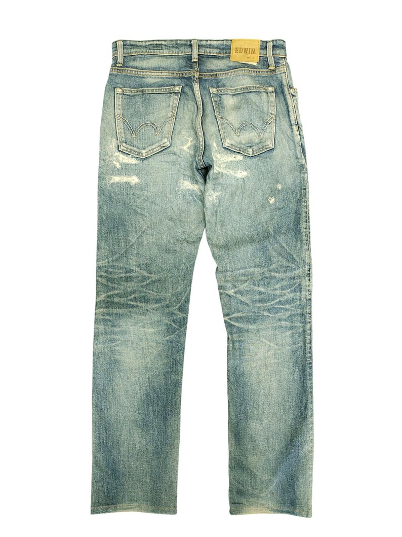 May include: Light blue denim jeans with a distressed look, featuring faded areas and worn details. The back view shows the pockets, belt loops, and a small "EDWIN" label. The jeans have a classic, straight-leg fit.