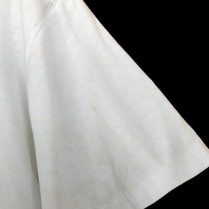 May include: Close-up of the white fabric sleeve of a t-shirt. The fabric is slightly creased and has a few faint marks.