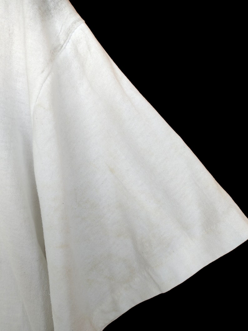 May include: Close-up of the white fabric sleeve of a t-shirt. The fabric is slightly creased and has a few faint marks.