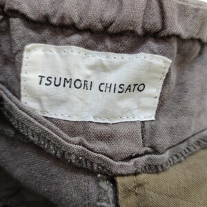 May include: A close-up of a gray fabric label with the text "TSUMORI CHISATO" in black lettering. The label is attached to a garment.
