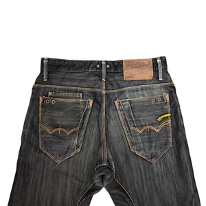 Op de afbeelding: Donkerblauwe denim jeans met oranje stiksels en een leren patch. De jeans heeft twee achterzakken met decoratieve stiksels en een gele accent. De merknaam Edwin is zichtbaar op de leren patch.