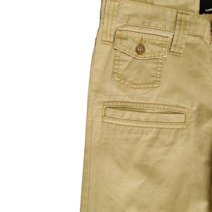 Puede incluir: Un pantal&oacute;n cargo color caqui con un bolsillo grande en el lado derecho. El bolsillo tiene un cierre de bot&oacute;n y est&aacute; acentuado con costuras.