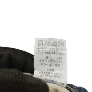 May include: A close-up of a clothing tag with Japanese text and care symbols. The tag lists the materials as 98% cotton and 2% polyurethane. The tag also includes the text "Made in Japan".