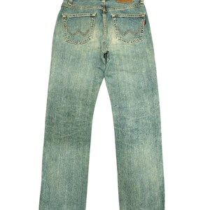 May include: Light blue denim jeans with a faded wash. The jeans feature classic five-pocket styling, a brown leather patch with the brand name, and decorative stitching on the back pockets. The jeans are a straight-leg style.