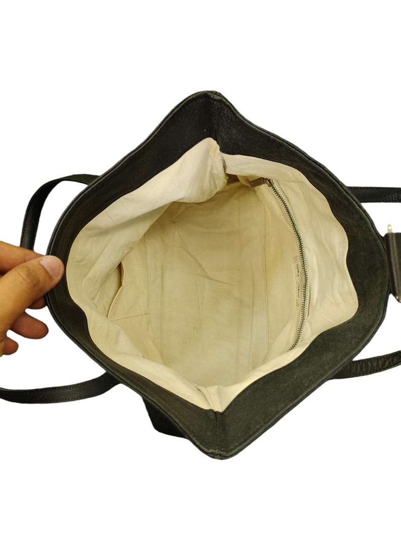 May include: A black leather tote bag with a cream coloured lining. The bag has a zipped pocket on the inside and two straps.