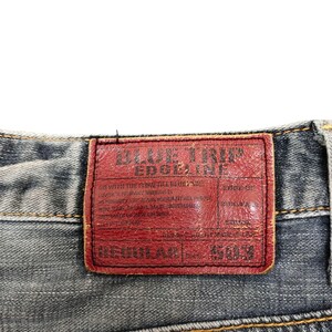May include: Close-up of the back of blue denim jeans. A red leather patch with the text "BLUE TRIP EDGELINE" is visible. The jeans have a regular fit and are stitched with yellow thread.