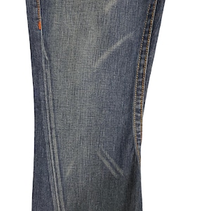 K&ouml;nnte beinhalten: Nahaufnahme des Jeansstoffes einer blauen Jeans mit einem kleinen Loch im Stoff. Die Jeans hat orangefarbene N&auml;hte entlang der N&auml;hte.