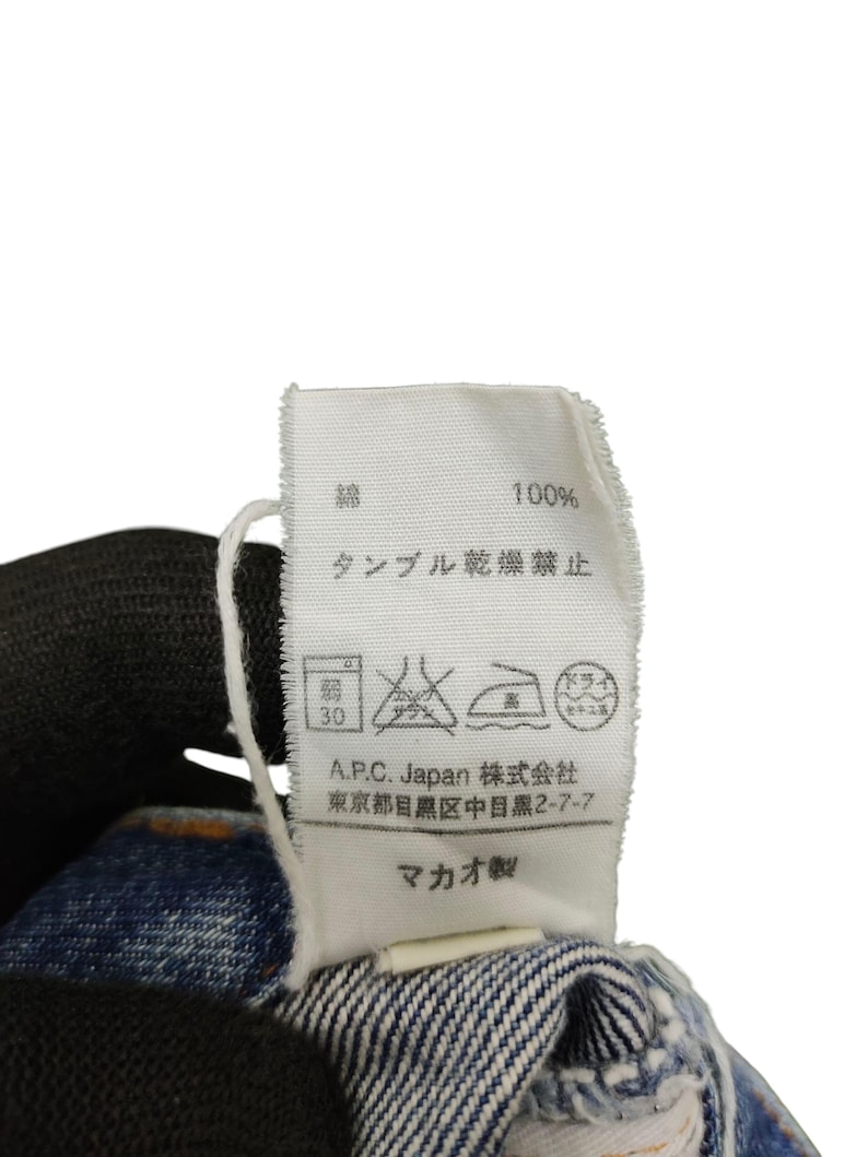 Puede incluir: Primer plano de una etiqueta de ropa blanca con texto japon&eacute;s y s&iacute;mbolos de cuidado. La etiqueta indica "100%" e instrucciones de lavado. Tambi&eacute;n se ve la marca "A.P.C. Japan".