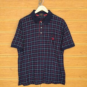 Könnte beinhalten: Ein marineblaues Poloshirt mit einem rot-weiß karierten Muster. Das Shirt hat einen Knopfkragenshirt und ein kleines gesticktes Logo auf der linken Brust.