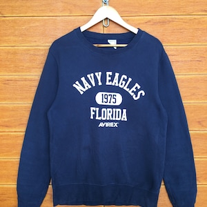 May include: Navy blue sweatshirt with white text that reads "Navy Eagles 1975 Florida Avirex".