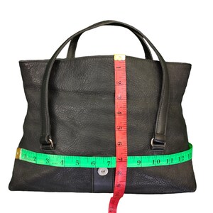 May include: Black leather tote bag with a top handle and a zipper closure. The bag is measured with a tape measure, showing the width is 30 cm and the height is 18 cm.