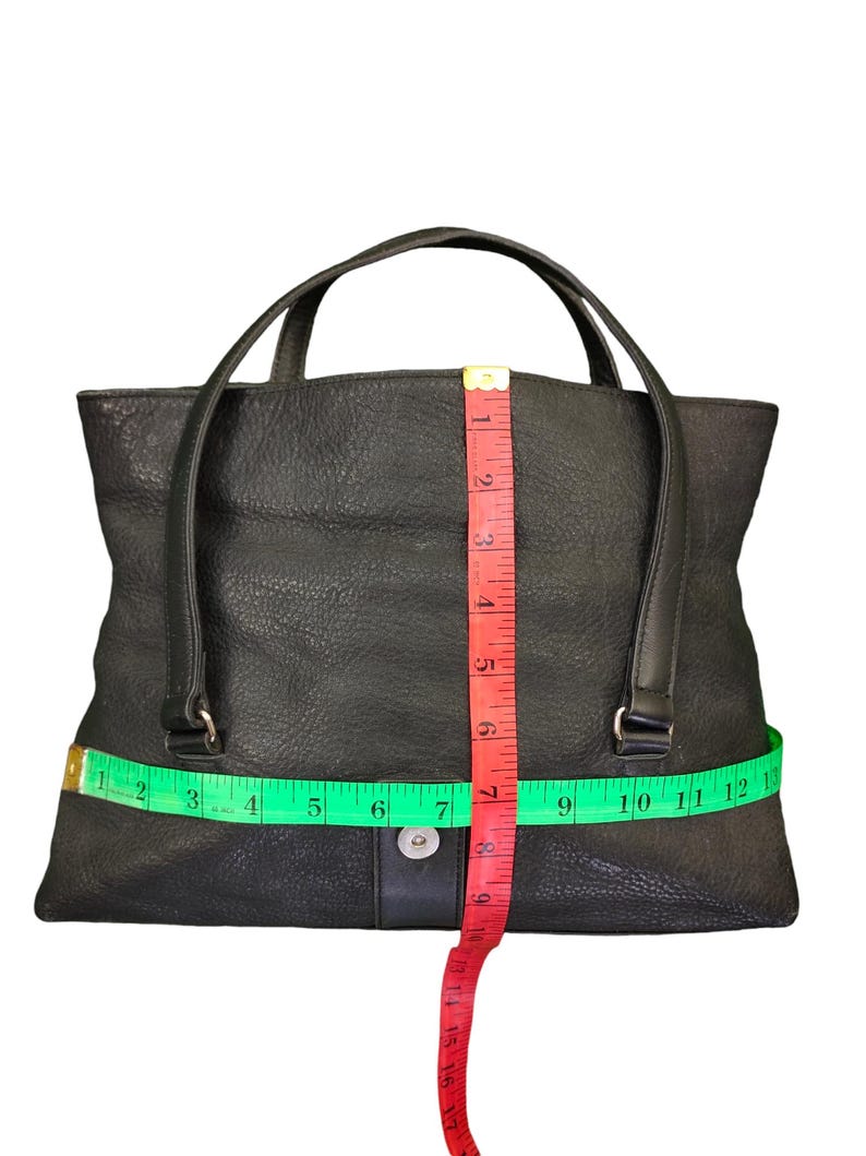 May include: Black leather tote bag with a top handle and a zipper closure. The bag is measured with a tape measure, showing the width is 30 cm and the height is 18 cm.