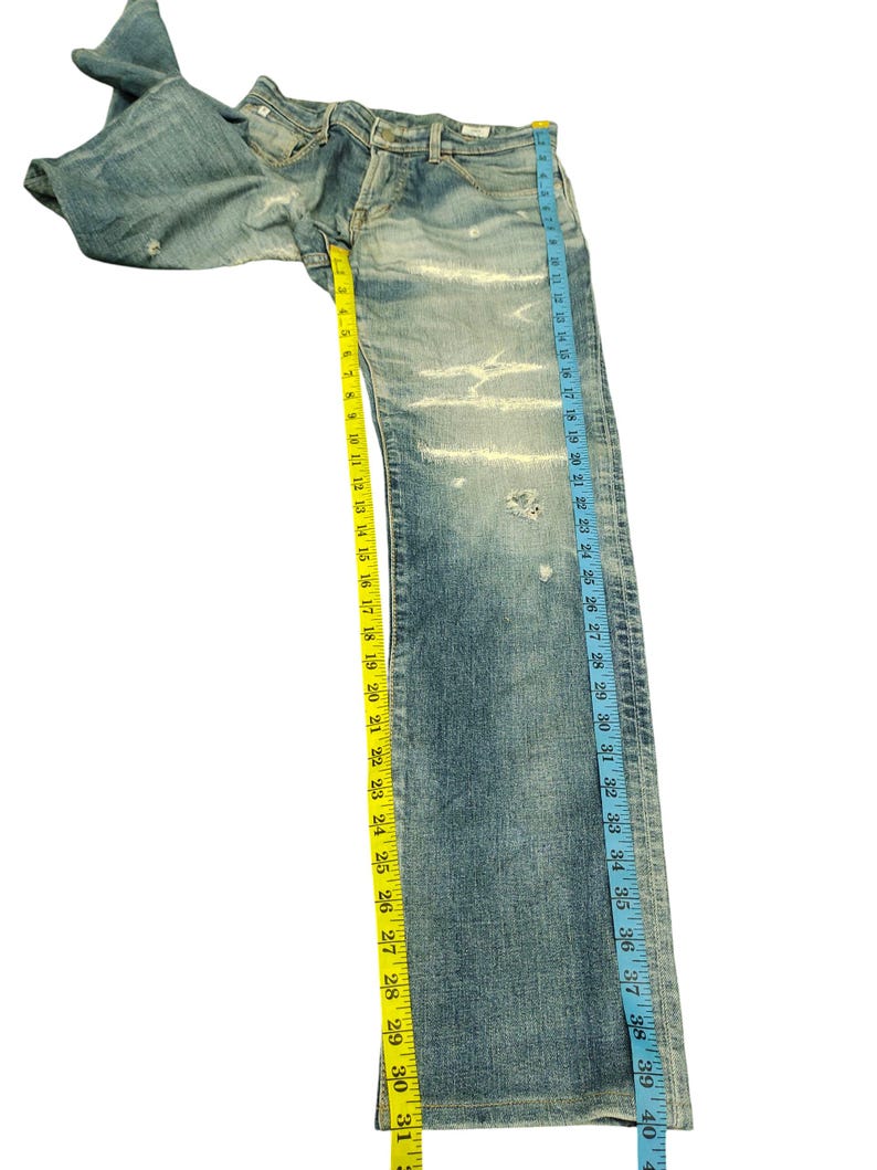 May include: Light blue denim jeans with distressed details, measuring approximately 40 inches in length. The jeans have a classic five-pocket design and are measured with a yellow and blue measuring tape.