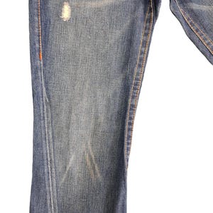May include: Close-up of the front of a pair of blue denim jeans with a small faded spot on the left leg.