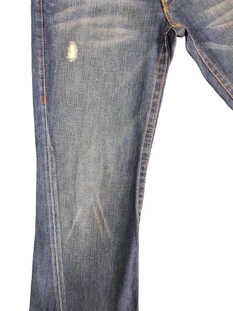 May include: Close-up of the front of a pair of blue denim jeans with a small faded spot on the left leg.