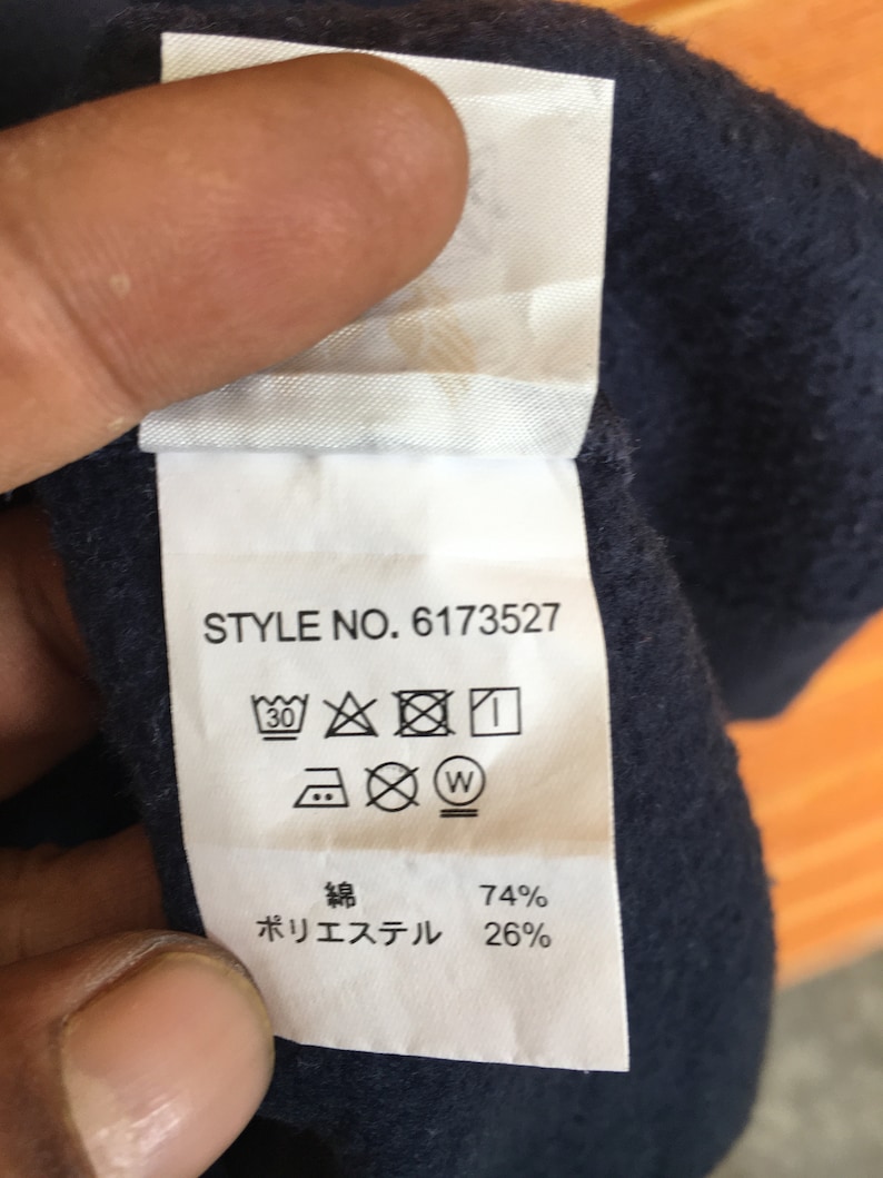 May include: A white care label with black text and symbols. The text reads "STYLE NO. 6173527" and "74% Polyester 26%". The symbols include a washing machine icon with a 30 degree symbol, an iron icon with a dot, a dry clean icon with a circle and a cross, and a tumble dry icon with a circle and a cross.