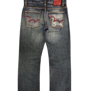 May include: Faded blue denim jeans with red stitching on the back pockets and a red leather patch. The jeans have a classic five-pocket design and a straight leg cut. The denim has a worn, distressed look.