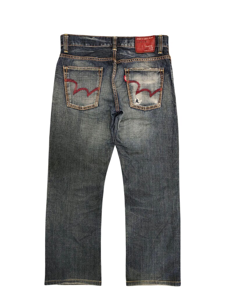 May include: Faded blue denim jeans with red stitching on the back pockets and a red leather patch. The jeans have a classic five-pocket design and a straight leg cut. The denim has a worn, distressed look.
