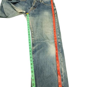 Puede incluir: Vaqueros de mezclilla azul claro con corte recto. Los vaqueros se miden con una cinta m&eacute;trica verde que muestra aproximadamente 71 cm y una cinta m&eacute;trica roja que muestra aproximadamente 97 cm.