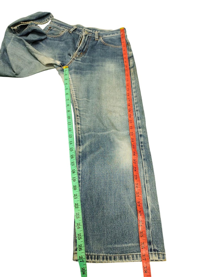 Puede incluir: Vaqueros de mezclilla azul claro con corte recto. Los vaqueros se miden con una cinta m&eacute;trica verde que muestra aproximadamente 71 cm y una cinta m&eacute;trica roja que muestra aproximadamente 97 cm.