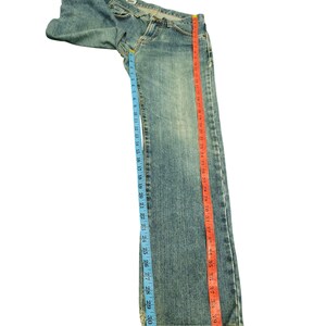 May include: Light blue denim jeans with a classic five-pocket design. The jeans are measured with a blue tape measure showing a 33-inch inseam and a red tape measure showing a 42-inch length. The jeans are laid flat on a white surface.