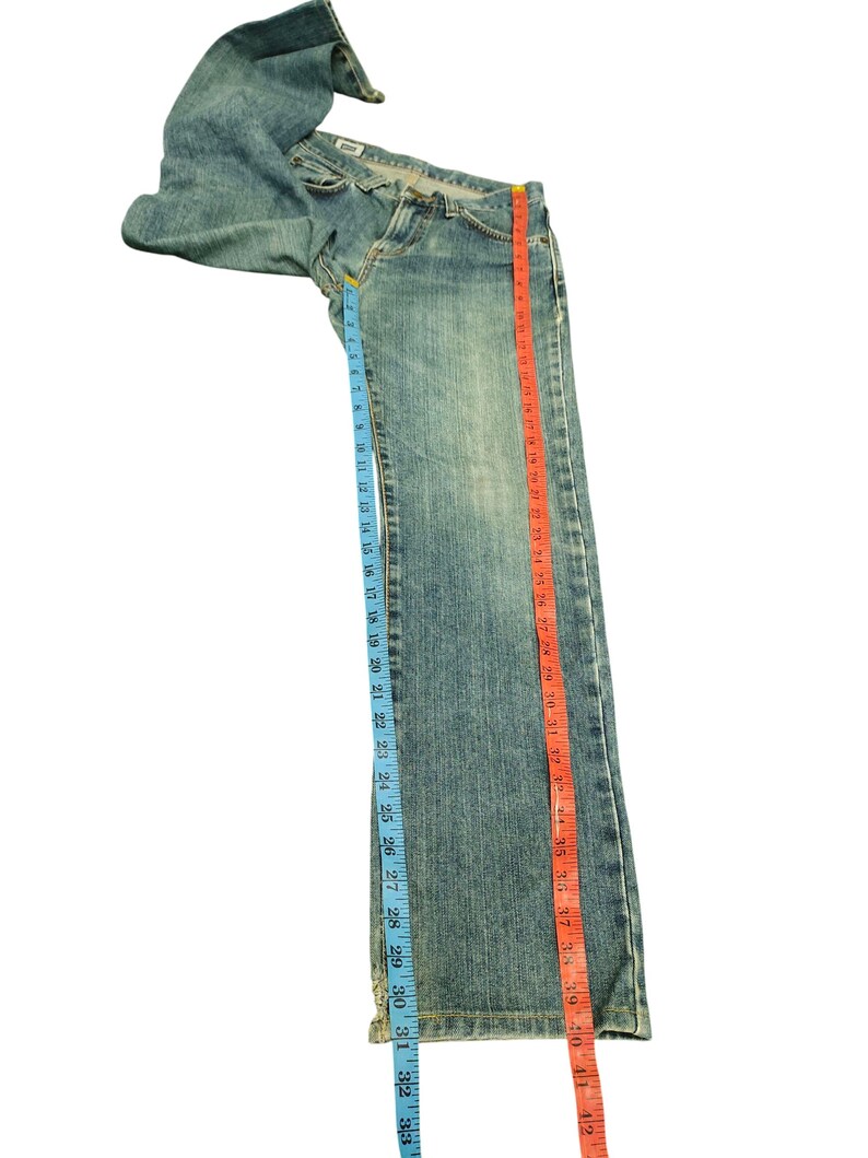 May include: Light blue denim jeans with a classic five-pocket design. The jeans are measured with a blue tape measure showing a 33-inch inseam and a red tape measure showing a 42-inch length. The jeans are laid flat on a white surface.