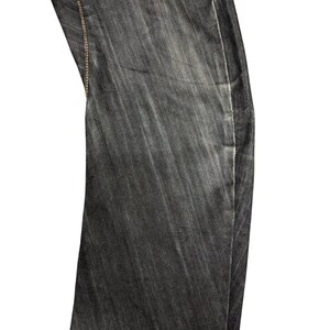 Op de afbeelding: Close-up van een gedeelte van een donkergrijze denim jeans. De stof heeft een subtiele verticale textuur en is gestikt met een contrasterend lichtbruin garen. De jeans lijken licht vervaagd, waardoor ze een versleten uitstraling hebben.