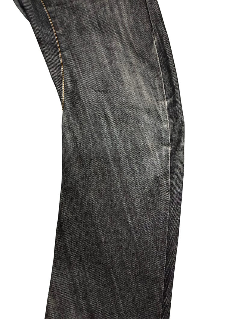 Op de afbeelding: Close-up van een gedeelte van een donkergrijze denim jeans. De stof heeft een subtiele verticale textuur en is gestikt met een contrasterend lichtbruin garen. De jeans lijken licht vervaagd, waardoor ze een versleten uitstraling hebben.