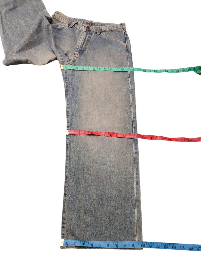 May include: Light blue denim jeans with a classic five-pocket design. A green measuring tape shows a waist measurement of approximately 22 inches. A red measuring tape shows an inseam measurement of approximately 17 inches. A blue measuring tape shows a leg opening of approximately 9 inches.