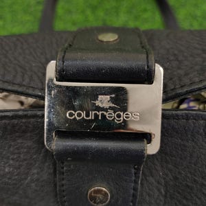 May include: A black leather handbag with a silver buckle and the word "courr&egrave;ges" embossed on it.