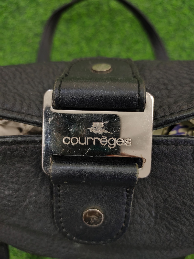 May include: A black leather handbag with a silver buckle and the word "courr&egrave;ges" embossed on it.