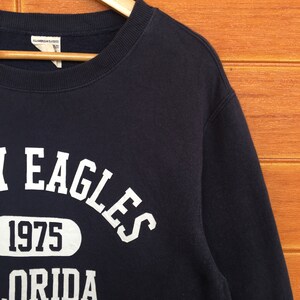 May include: A black sweatshirt with white text that reads "EAGLES 1975 FLORIDA AVIREX".
