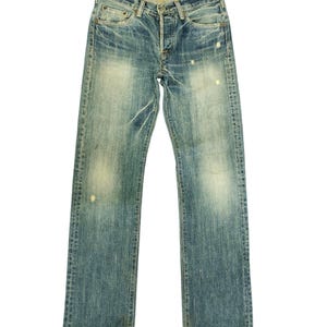 Puede incluir: Vaqueros de mezclilla azul descolorido con bragueta de botones y dise&ntilde;o cl&aacute;sico de cinco bolsillos. Los vaqueros tienen un aspecto desgastado con decoloraci&oacute;n clara y marcas de uso, d&aacute;ndoles una est&eacute;tica vintage. El dobladillo est&aacute; ligeramente deshilachado.