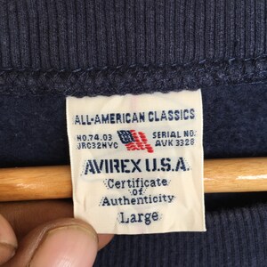 May include: A navy blue sweatshirt with a white tag that reads "ALL-AMERICAN CLASSICS", "NO.74.03 JRC32NVC", "SERIAL NO. AUK 3328", "AVIREX U.S.A.", "Certificate of Authenticity", and "Large".
