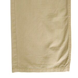 Puede incluir: Primer plano del dobladillo inferior de un pantal&oacute;n caqui. La tela es de algod&oacute;n tejido liso con una textura sutil. El dobladillo est&aacute; acabado con una doble fila de costuras.