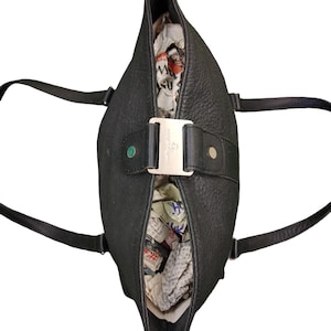 May include: A black leather tote bag with a silver buckle and a small green tag. The bag is open and filled with crumpled paper.